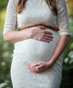 Schwangere Frau im weißen Kleid hält ihren Bauch