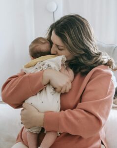 Mama mit Baby auf dem Arm sitzt auf dem Bett.